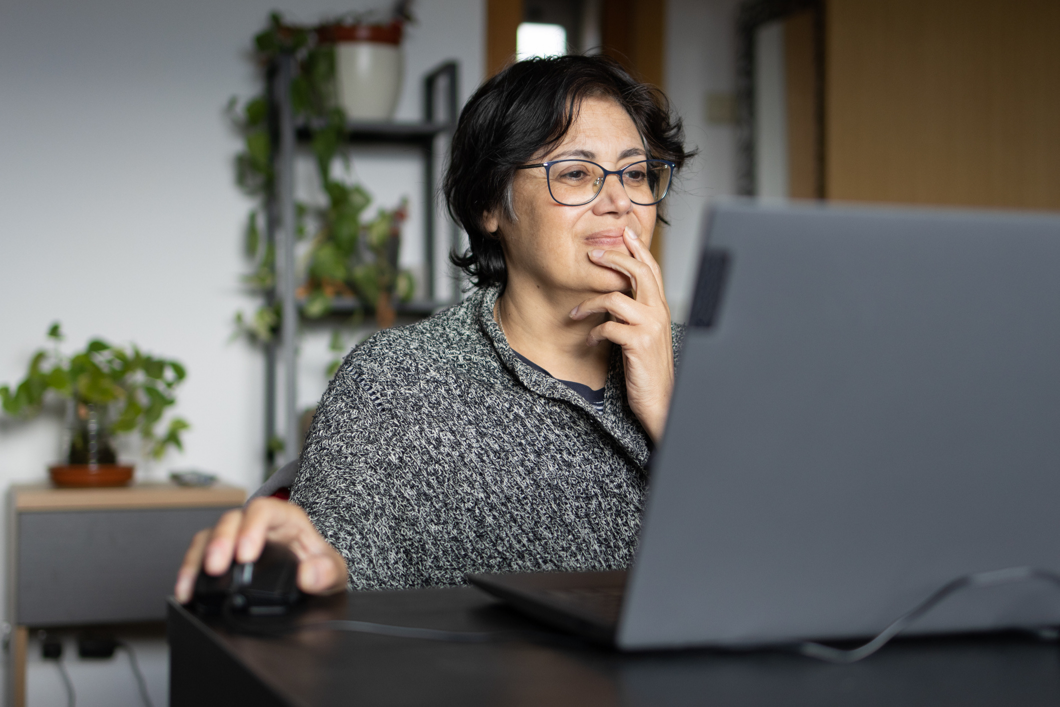A woman holds her face while searching on her computer for benefits at home.
