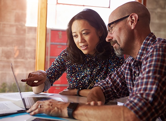 A man and a woman working together on a laptop computer.