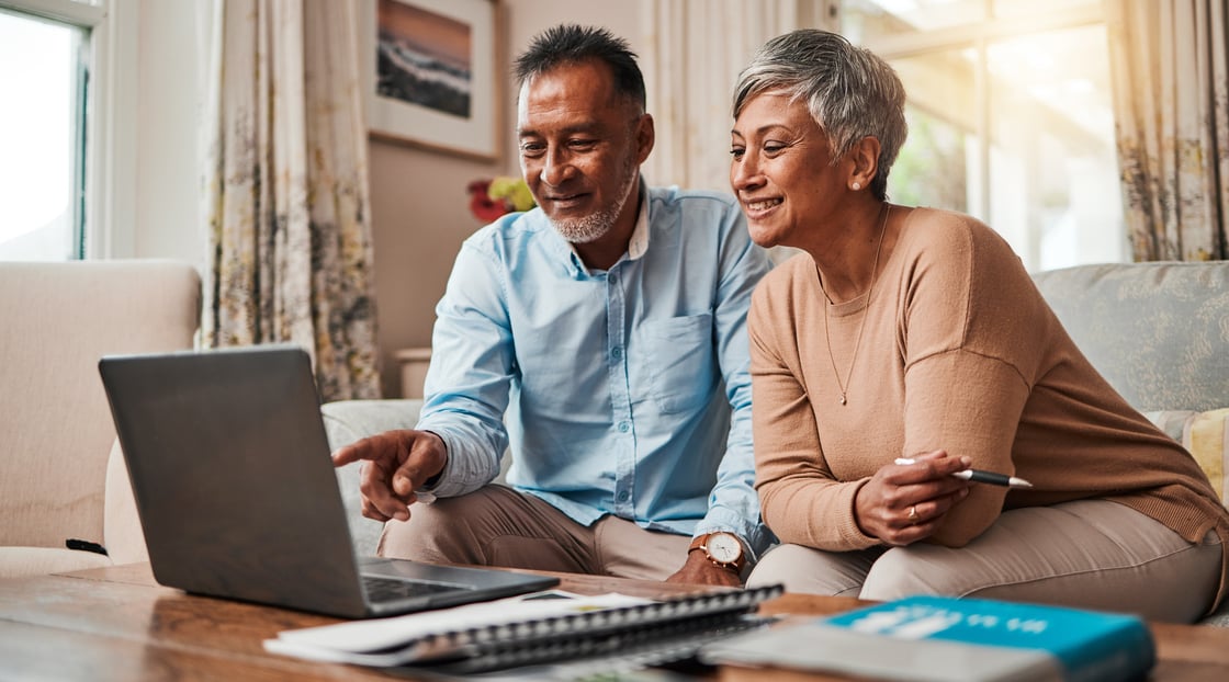 Elderly couple reading information on computer on their couch with papers on the sofa table.-1