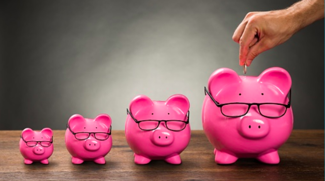 Four piggy banks in a row, a hand drops a coin into the final and largest piggy bank