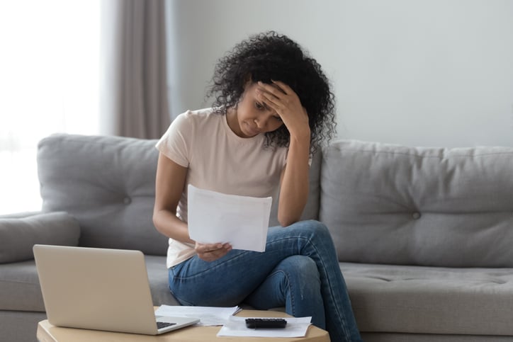 Stressed woman sits on couch holding bills worried