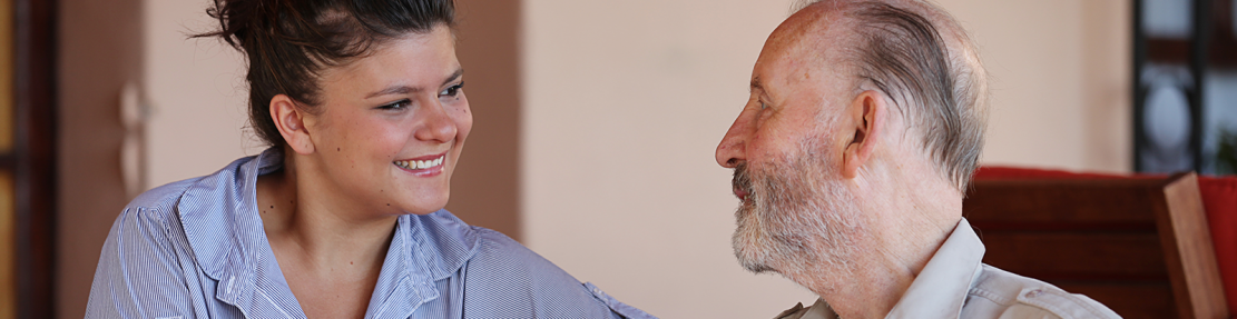 A young woman smiles at an older man who is seated.