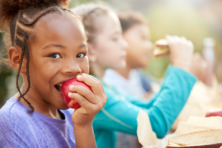 A young girl smiles and eats an apple at a summer gathering with friends.