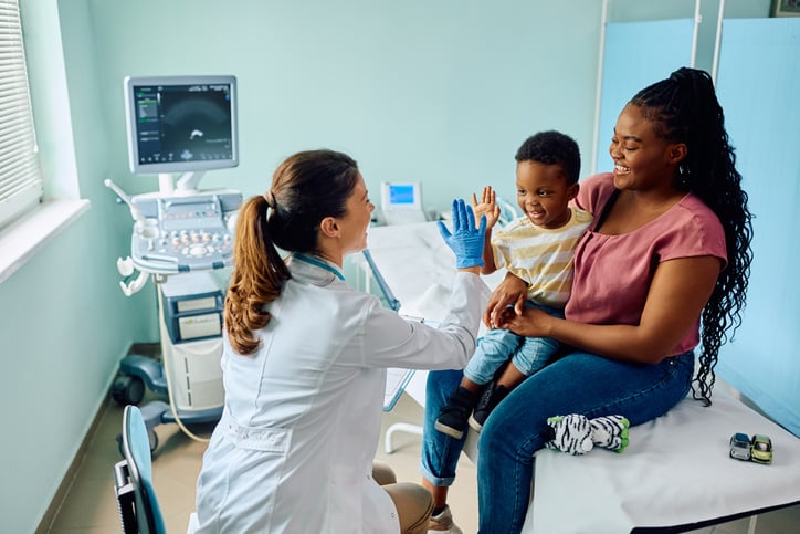 A doctor gives a toddler a high-five for being brave while getting a health check up in a doctor's office.